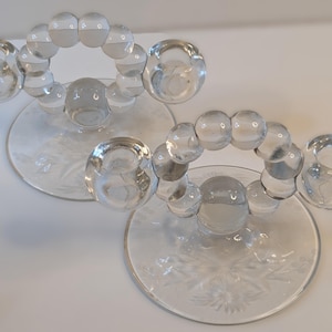 May include: A white ceramic mug with a black handle and the text "But First, Coffee" in a bold, black font. The mug is set against a blurred background, suggesting a cozy setting.