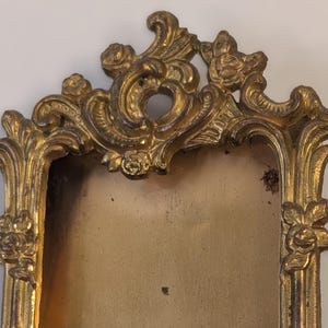 May include: Ornate gold-colored picture frame with a rectangular opening. The frame features elaborate scrollwork and floral accents, with a distressed finish. The frame is designed in a vintage style.