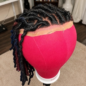 May include: A red mannequin head with black, blue, and burgundy dreadlocks. The dreadlocks are styled with a lace front. The mannequin head is mounted on a black stand.
