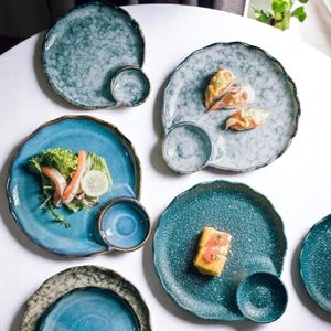 May include: Set of six blue and white ceramic plates with a small dipping bowl attached to each plate. The plates have a speckled glaze and a wavy edge.