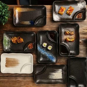 May include: A set of ten black and white ceramic plates with different designs. The plates have a divided section for dipping sauces or condiments. Some plates have a brushstroke design, while others have a more traditional look.