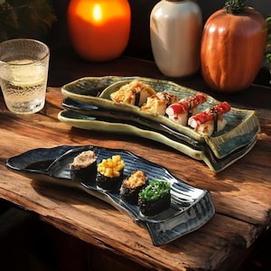 May include: A set of four blue and green ceramic sushi plates. The plates are shaped like a crescent moon and have a textured surface. The plates are filled with various types of sushi, including nigiri, maki, and sashimi.