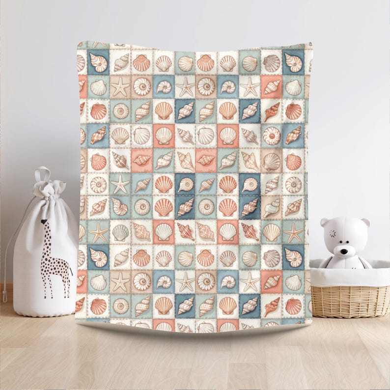 Puede incluir: Una manta estampada cuadrada con un dise&ntilde;o repetido de conchas marinas y estrellas de mar en tonos melocot&oacute;n, azul y crema. La manta se muestra sobre un fondo neutro, lo que sugiere un tema costero o de playa.
