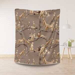 Peut inclure: Une couverture marron avec un motif r&eacute;p&eacute;t&eacute; de lions, de gu&eacute;pards et de leurs petits sur des branches d'arbres. Le motif est de style aquarelle avec une palette de couleurs neutres, cr&eacute;ant un th&egrave;me safari.