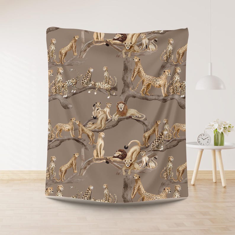 Peut inclure: Une couverture marron avec un motif r&eacute;p&eacute;t&eacute; de lions, de gu&eacute;pards et de leurs petits sur des branches d'arbres. Le motif est de style aquarelle avec une palette de couleurs neutres, cr&eacute;ant un th&egrave;me safari.