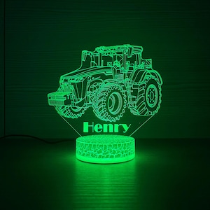 Op de afbeelding: Een groen oplichtend nachtlampje in de vorm van een tractor met de naam "Henry" aan de basis. Het tractorontwerp toont gedetailleerde contouren van de componenten van het voertuig, inclusief wielen en cabine. De basis heeft een patroon van gebarsten aarde.