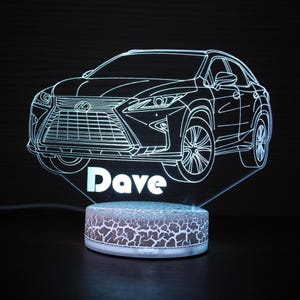 May include: A 3D LED night light featuring a car outline with the name "Dave" illuminated in white. The base has a cracked earth design. The car is a detailed line drawing.