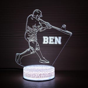 Op de afbeelding: Een LED-nachtlampje met honkbalthema, met een honkballer in actie en de naam "BEN". De ronde basis heeft een textuurpatroon en straalt een zachte gloed uit, perfect voor een slaapkamer of sportkamer.