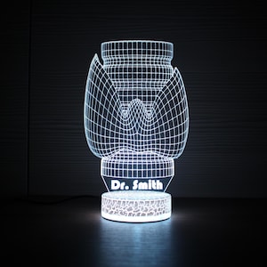 May include: A glowing white 3D-printed lamp in the shape of a thyroid gland. The lamp has a grid-like design and sits on a round base with the name "Dr. Smith" displayed. The base has a decorative pattern.