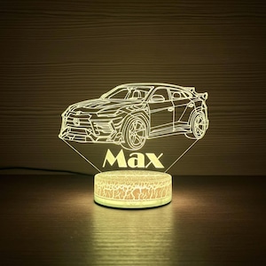 Könnte beinhalten: Eine leuchtende LED-Nachtlampe mit einem Auto-Design und dem Namen "Max". Das Auto ist detailliert dargestellt, und der Sockel hat eine rissige Textur. Das Licht strahlt warm. Geeignet für ein Schlafzimmer.