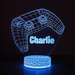 May include: A blue LED night light shaped like a video game controller. The name "Charlie" is displayed in white. The base has a cracked pattern.
