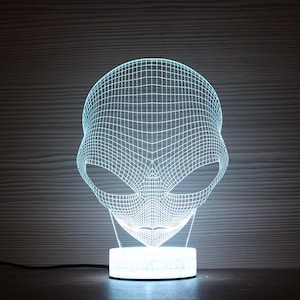 Könnte beinhalten: Eine weiße 3D-gedruckte Alien-Kopflampe mit einem Drahtgitterdesign. Die Lampe steht auf einem weißen Sockel mit einem schwarzen Kabel.
