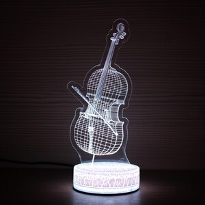 May include: A white 3D printed cello shaped night light with a clear base. The cello is illuminated from within, creating a glowing effect.