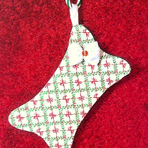 May include: A Christmas stocking with a white background, decorated with a pattern of red bows, green holly, and red berries. A white bow with a red center is attached. The stocking has a candy cane-striped loop for hanging.
