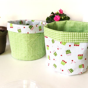 May include: Two fabric storage baskets, one green with white gingham pattern and one white with green gingham trim and a pattern of red and pink flowers.