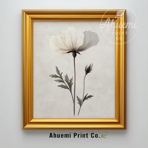May include: A framed botanical print featuring a white flower with a dark center and a bud, set against a neutral background. The artwork is enclosed in a gold frame. The text "Ahuemi Print Co." is visible at the bottom.