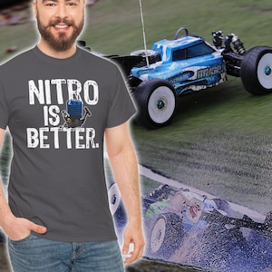 Może przedstawiać: Szary t-shirt z napisem "NITRO IS BETTER." w kolorze białym z kreskówkową ilustracją silnika nitro. Koszulkę nosi osoba. W tle znajduje się niebieski i biały samochód zdalnie sterowany.