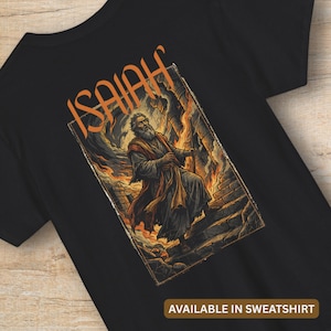 Può includere: T-shirt nera con un'illustrazione di un uomo barbuto in una veste, con la parola "ISAIAH" in arancione sopra l'immagine. L'opera d'arte raffigura una scena biblica con fiamme e una struttura in pietra. Il testo "AVAILABLE IN SWEATSHIRT" è in basso.