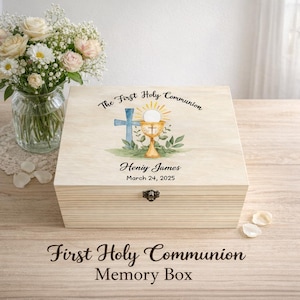 May include: A light-coloured wooden memory box with a hinged lid. The lid features a watercolour design of a cross, chalice, and text that reads "The First Holy Communion", the name "Heniy James", and the date "March 24, 2025". The box is labelled "First Holy Communion Memory Box".