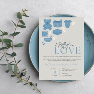 Puede incluir: Una invitación a un baby shower con un esquema de color azul claro y gris. La invitación presenta ilustraciones de artículos para bebés como un osito de peluche, una cesta y un body. El texto dice "Nestled in Love" e incluye los detalles del evento.