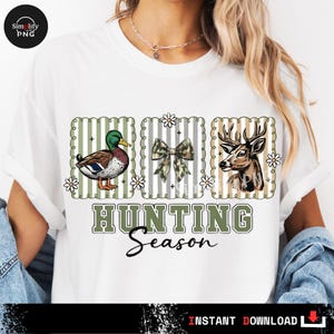 May include: White t-shirt with a hunting theme. The design includes a duck, a bow, and a deer, each within a decorative frame. The words "HUNTING Season" are printed in a green and black font.