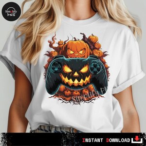 May include: White t-shirt featuring a Halloween-themed design. The graphic includes a black video game controller with a jack-o'-lantern face, surrounded by orange pumpkins. The text "Simplify PNG" is visible.