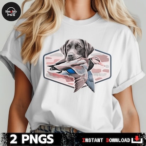 Op de afbeelding: Wit T-shirt met een afbeelding van een Labrador Retriever die een eend vasthoudt. Het ontwerp is geplaatst in een zeshoekige lijst met een camouflagepatroon. De tekst "2 PNGS" en "INSTANT DOWNLOAD" staan onderaan.