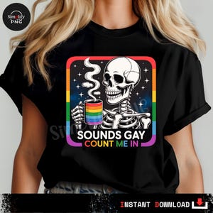 May include: Black t-shirt featuring a skeleton holding a rainbow-colored mug with steam rising. The design includes the text "SOUNDS GAY COUNT ME IN" in a colorful, square frame with a rainbow border.