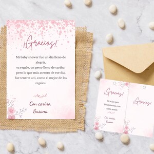 May include: Pink baby shower thank you cards with floral accents and the word "Gracias!" in script. The cards are on a burlap surface with a kraft paper envelope and decorative accents.