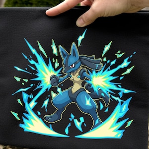 Könnte beinhalten: Schwarze quadratische Tasche mit einer blau-gelben Cartoonfigur, die von Energieexplosionen umgeben ist. Die Figur befindet sich in einer Kampfhaltung, mit blauen und gelben Energieeffekten. Die Tasche wird von einer Hand gehalten.