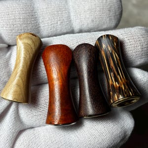 Op de afbeelding: Vier houten pijpstelen in verschillende tinten bruin en beige. De stelen hebben een gebogen zandloper vorm en zijn gemaakt van verschillende soorten hout, waaronder licht beige, roodbruin, donkerbruin en een bruin met patronen.