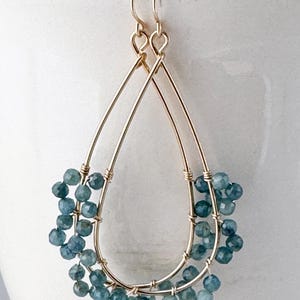 Puede incluir: Pendientes de gota de oro con cuentas de piedras preciosas azules. Los pendientes están hechos con dos alambres finos de oro que están envueltos alrededor de las cuentas.