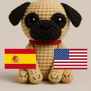 May include: A crocheted pug plush toy holding a Spanish flag in its left paw and an American flag in its right paw. The plush toy is tan with black eyes and a red collar.