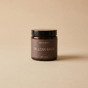 Könnte beinhalten: Ein dunkel bernsteinfarbenes Glasgefäß mit schwarzem Schraubdeckel und einem braunen Etikett, auf dem der Text simply glow, TALLOW BASIC und 50ml of Balm in Weiß gedruckt ist. Der Behälter ist zylindrisch und enthält ein Hautpflegeprodukt.