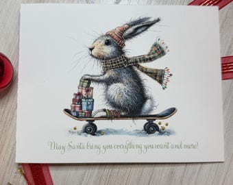 May include: A Christmas card featuring a gray rabbit wearing a hat and scarf, riding a skateboard and carrying gifts. The card has the text "May Santa bring you everything you want and more!" in a script font. The card is on a light wood surface.