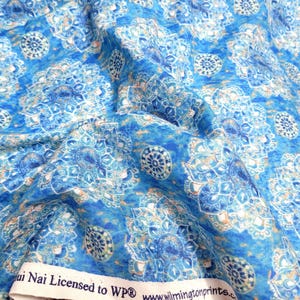 Peut inclure: Gros plan sur un tissu bleu avec un motif répétitif de motifs floraux blancs et bleu clair. Le tissu a un aspect texturé et un léger éclat. Le tissu est étiqueté "ai Nai Licensed to WP".