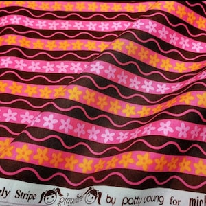 Puede incluir: Tela estampada con flores rosas y naranjas y rayas marrones onduladas sobre un fondo rosa. La tela tiene el texto "Squiggly Stripe" y "play" en la parte inferior.