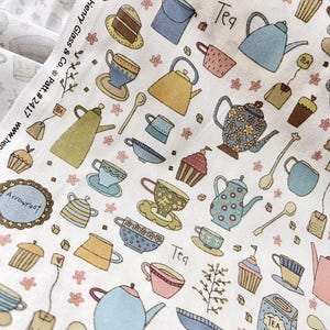 May include: White fabric with a repeating pattern of teacups, teapots, cupcakes, and tea-related items in pastel colors. The word "Tea" is visible in the design. The fabric is marked "Patched for Henry Glass & Co."