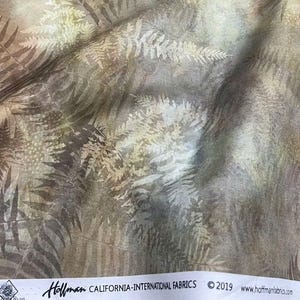 Op de afbeelding: Een stuk stof met een gelaagd varenbladpatroon in tinten bruin, beige en crème. De zelfkant toont de tekst Hoffman California-International Fabrics, 2019, en het websiteadres www.hoffmanfabrics.com.