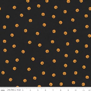 May include: A black fabric featuring a repeating pattern of small orange jack-o'-lanterns with carved faces. A white ruler at the bottom edge shows a scale of 12 inches, with the text Riley Blake Designs printed near the 2-inch mark.