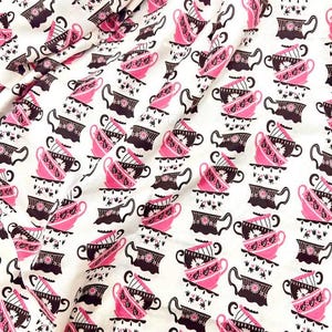 Puede incluir: Tela blanca con un patrón repetido de tazas de té rosas y negras. Las tazas de té están apiladas y decoradas con diseños florales y geométricos. La tela está doblada, creando sombras y profundidad.