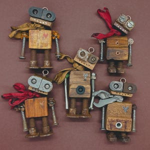 Puede incluir: Una colección de cinco figuras de robots de madera hechas a mano. Cada robot tiene un cuerpo de bloque de madera, piernas y brazos de pernos metálicos y una cabeza de metal y madera. Algunos robots tienen bufandas de tela en rojo, beige y gris.