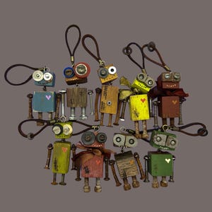 May include: A collection of handmade robot keychains. Each robot is crafted from wood and metal hardware, featuring painted bodies in various colors like blue, yellow, and green. They have button eyes and heart accents, with brown leather loop attachments.