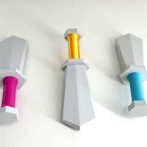 May include: Three decorative sword-shaped objects with gray blades and white hexagonal bases. One has a pink handle, one a gold handle, and the third a blue handle. The objects are displayed against a white background.