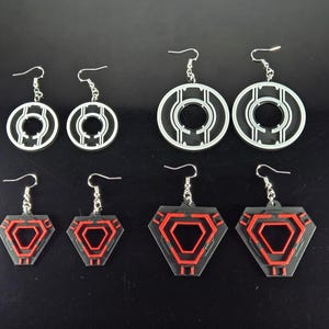 May include: A collection of six pairs of earrings in various geometric designs. The earrings feature silver hooks and are made of black and red acrylic. The designs include circular and hexagonal shapes.