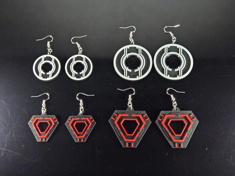 May include: A collection of six pairs of earrings in various geometric designs. The earrings feature silver hooks and are made of black and red acrylic. The designs include circular and hexagonal shapes.