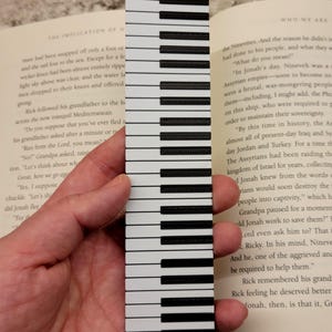 May include: A black and white piano keyboard bookmark. The bookmark is made of a durable material and features a realistic piano keyboard design.