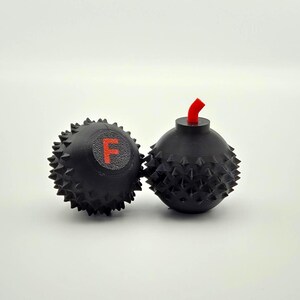 May include: Two black, spiky, novelty items resembling bombs. One has a red "F" on it, the other has a red fuse. The items are likely decorative or gag gifts. The objects are on a white background.