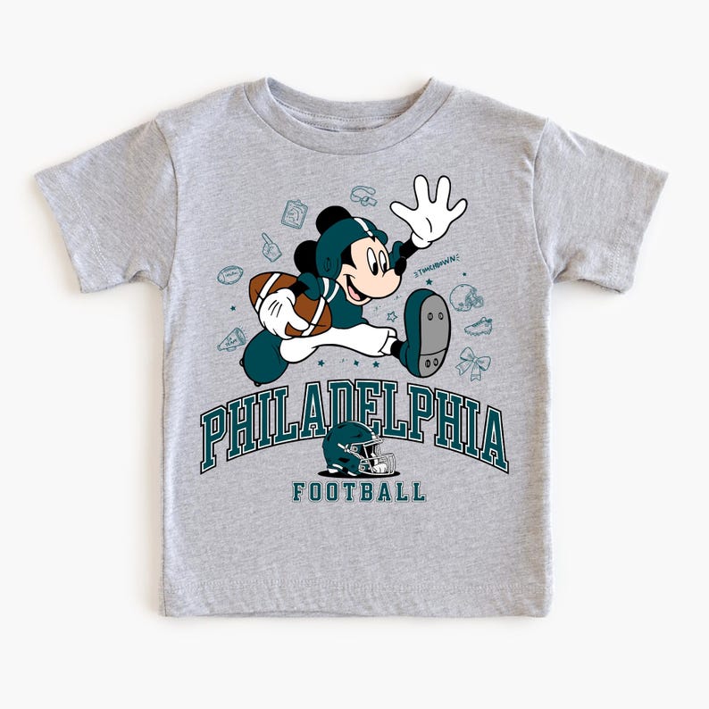 A gray t-shirt with a graphic design featuring a cartoon character in a football uniform, along with various football-related icons and text.