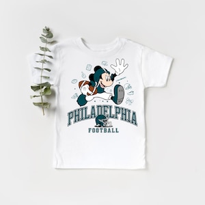 A white t-shirt with a graphic design featuring a cartoon character and text related to Philadelphia Football.